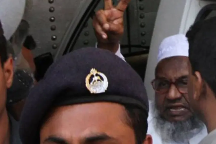 Abdul Quader Molla faz sinal de vitória ao andar com policiais: Supremo revisou a pena inicial de Abdul Quader Molla, dirigente do partido Jamaat-e-Islami, que era de prisão perpétua (AFP)