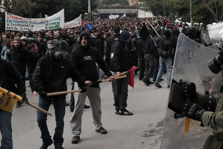 
	Manisfestantes s&atilde;o observados pela pol&iacute;cia em Atenas: uma grande manifesta&ccedil;&atilde;o ocorreu no s&aacute;bado para protestar contra as expuls&otilde;es durante o fim de semana
 (Louisa Gouliamaki/AFP)