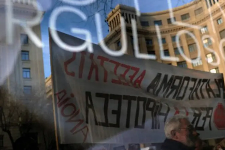 
	Manifestantes em frente &agrave; vidra&ccedil;a que diz &quot;Orgulhosos&quot; em Barcelona: a redu&ccedil;&atilde;o &eacute; uma amostra do relaxamento dos mercados, embora a d&iacute;vida ainda seja elevada
 (Lluis Gene/AFP)