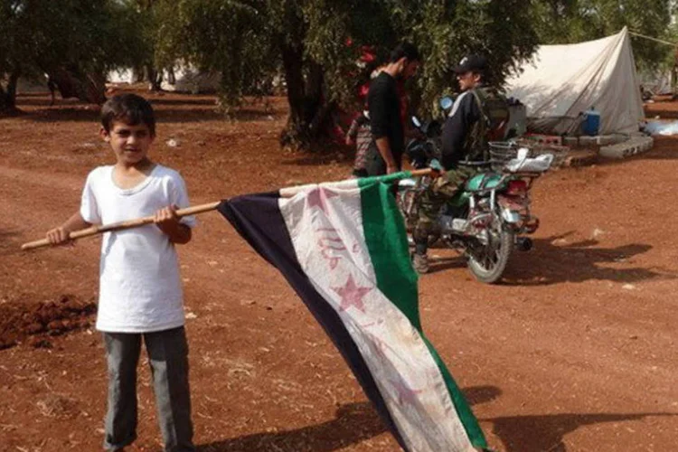 
	Refugiado s&iacute;rio balan&ccedil;a uma bandeira rebelde em um campo de Idleb: tr&ecirc;s carros-bombas explodiram
 (Herve Bar/AFP)