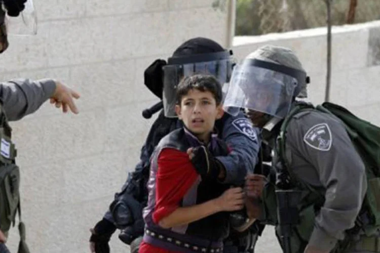 
	Policiais israelenses det&ecirc;m menino palestino durante um protesto em um campo de refugiados: a partir dos 14, as crian&ccedil;as podem ser condenadas a at&eacute; 10 anos por lan&ccedil;ar pedras
 (Musa al Shaer/AFP)