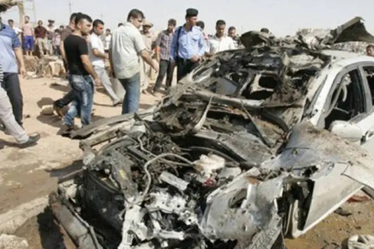 
	Policiais e civis iraquianos observam carro destru&iacute;do ap&oacute;s atentado em Kirkuk: o ataque, executado por um terrorista em um carro-bomba, tinha como alvo a delegacia de Dibis
 (Marwan Ibrahim/AFP)
