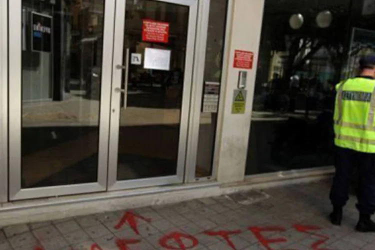 
	Policial em frente a banco de Nic&oacute;sia ao lado de grafite onde se l&ecirc; &quot;ladr&otilde;es&quot;: credores querem que o Chipre cobre taxas sobre os dep&oacute;sitos banc&aacute;rios em troca de resgate
 (Patrick Baz/AFP)
