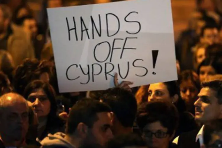 
	Manifestante cipriota mostra cartaz onde se l&ecirc; &quot;Tirem as m&atilde;os do Chipre&quot;, em frente ao Parlamento em Nic&oacute;sia: o mal-estar com a ilha j&aacute; se expressa abertamente
 (Patrick Baz/AFP)