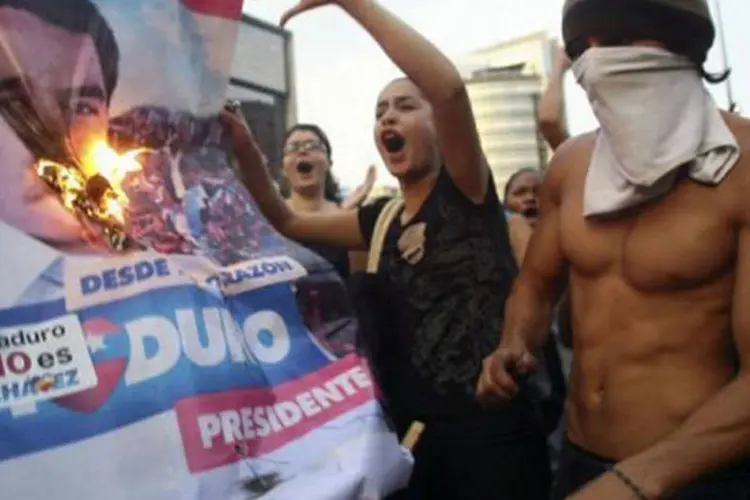 
	Simpatizantes de Capriles queimam um cartaz com a imagem de Maduro: os protestos come&ccedil;aram &nbsp;depois de o CNE ter proclamado Maduro presidente eleito, com 50,75% dos votos
 (Geraldo Caso/AFP)