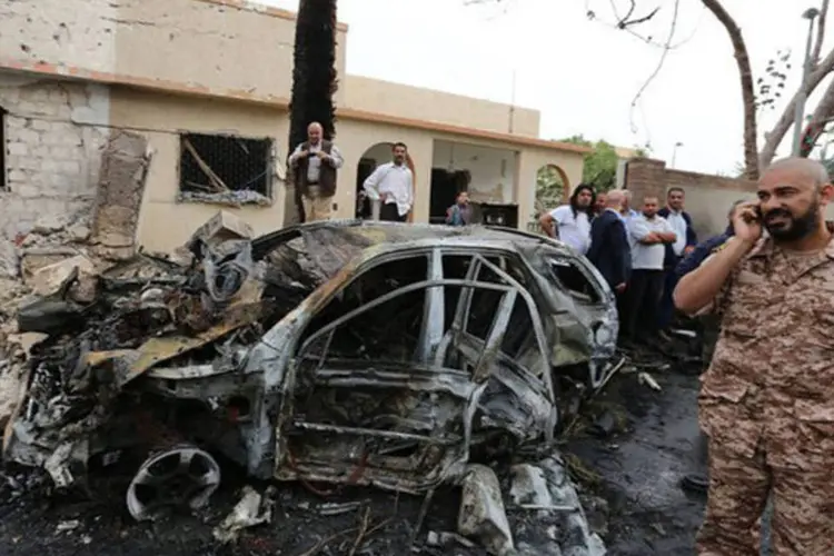 Forças de segurança líbias e civis observam veículo destruído após atentado em Trípoli (Mahmud Turkia/AFP)