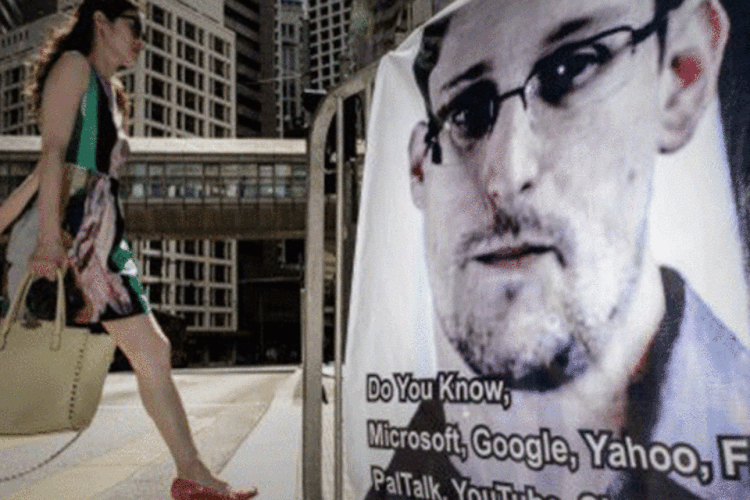 
	Uma mulher caminha ao lado de um banner de apoio a Edward Snowden, em Hong Kong: ex-agente poderia estar com viagem marcada para Cuba
 (Philippe Lopez/AFP)