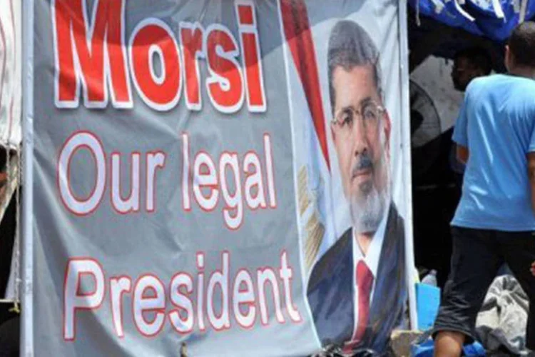 Jovem egípcio caminha ao lado de um retrato do presidente deposto do país, Mohamed Mursi: "redes se preocupam mais em comunicar os pontos de vista de seus sócios capitalistas do que em informar de maneira profissional e objetiva", afirma analista (Fayez Nureldine/AFP)