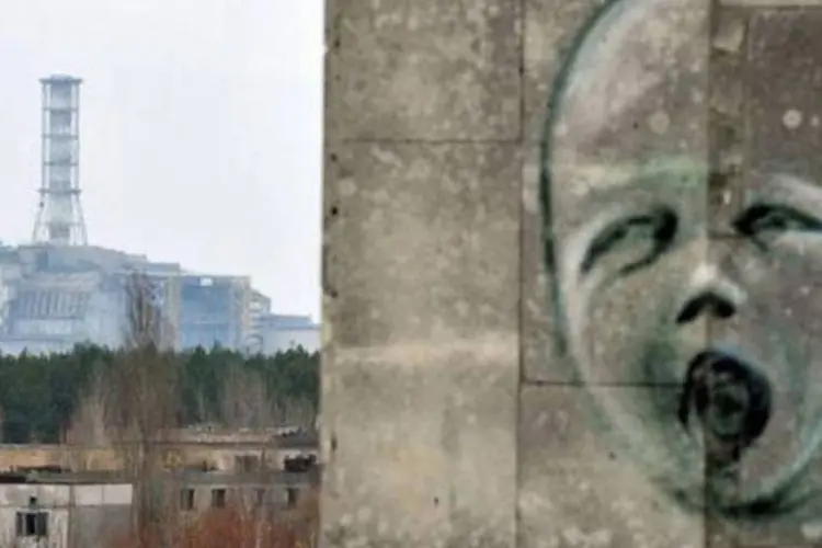 Pichação no muro da cidade fantasma de Pripyat com o prédio do reator 4 de Chernobyl ao fundo (Sergei Supinsky/AFP)