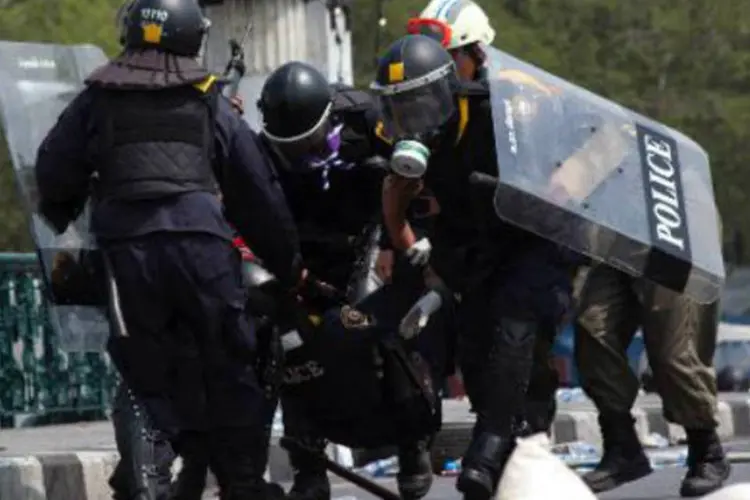 Policiais carregam um colega ferido por uma granada lançada por manifestantes, em Bangcoc: decisão provavelmente complicará ainda mais a ação do governo (KC Ortiz/AFP)