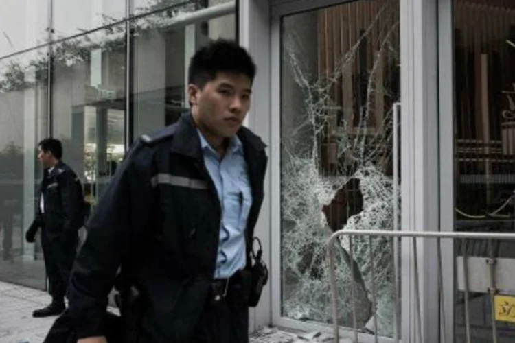 Policial passa por janela quebrada em prédio do governo no distrito de Admiralty, Hong Kong (Philippe Lopez/AFP)