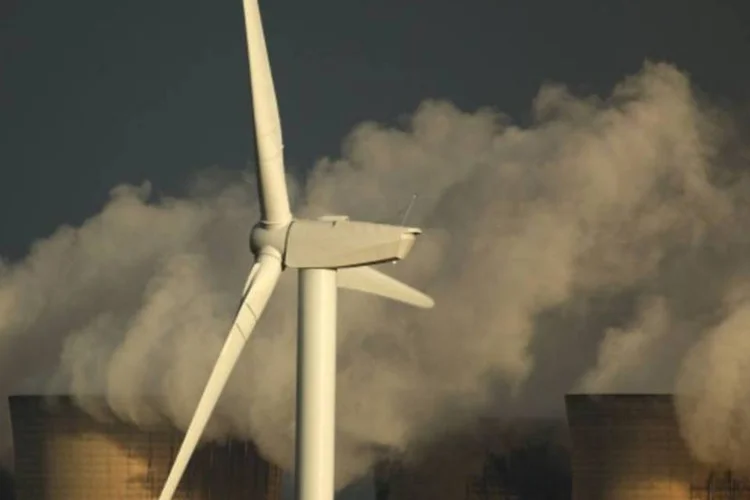 Poluição saindo de uma fábrica ao fundo de uma turbina eólica. (Christopher Furlong/Getty Images)
