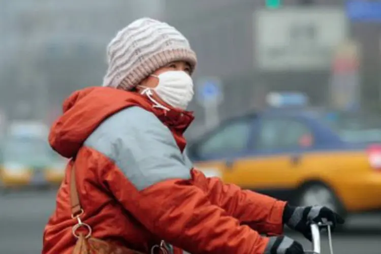 Chinesa anda de bicicleta com máscara para se proteger da poluição na capital, Pequim (Frederic J. Brown/AFP)