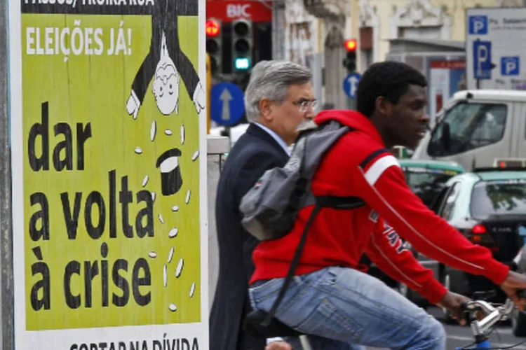Pessoas passam em frente a cartaz com protesto contra as políticas de austeridade adotadas por Portugal (REUTERS/Jose Manuel Ribeiro)