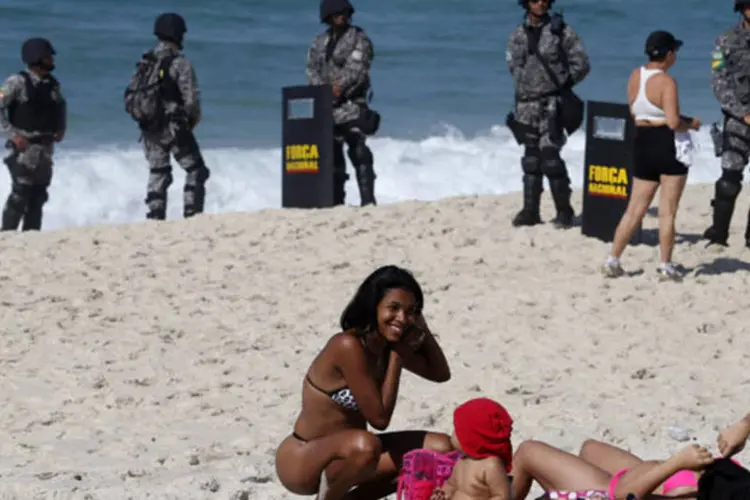 
	Mulheres tomam sol perto soldados da For&ccedil;a Nacional: bombas lan&ccedil;adas por policiais atingiram a areia da praia
 (REUTERS/Sergio Moraes)