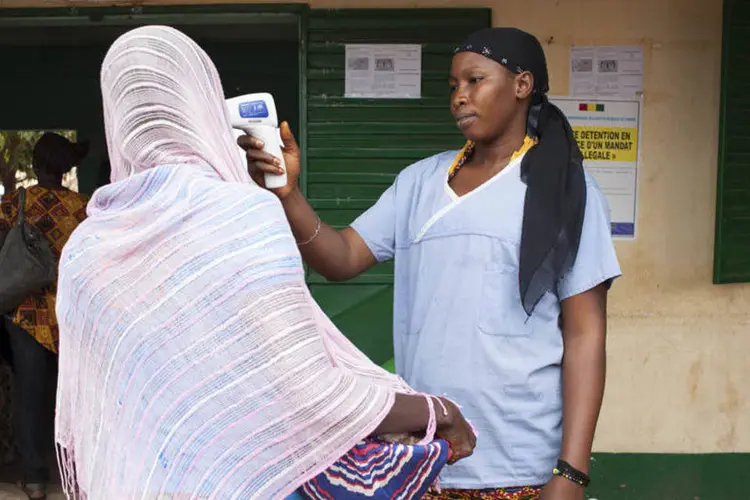 Profissional de saúde verifica temperatura em mulher que deixou Guiné, na fronteira com Mali , em Kouremale (Joe Penney/Reuters)