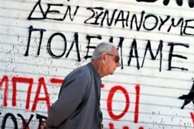 Em Atenas, homem caminha perto de muro onde se lê "eu não concordo - estamos em guerra". (.)