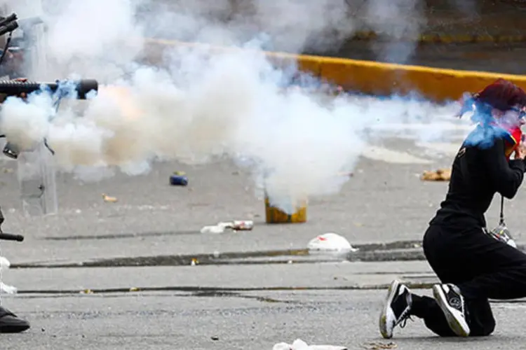 Polícia da Venezuela dispara gás lacrimogêneo enquanto manifestante cai de joelhos segurando uma pedra durante confronto em Caracas (REUTERS/Carlos Garcia Rawlins)