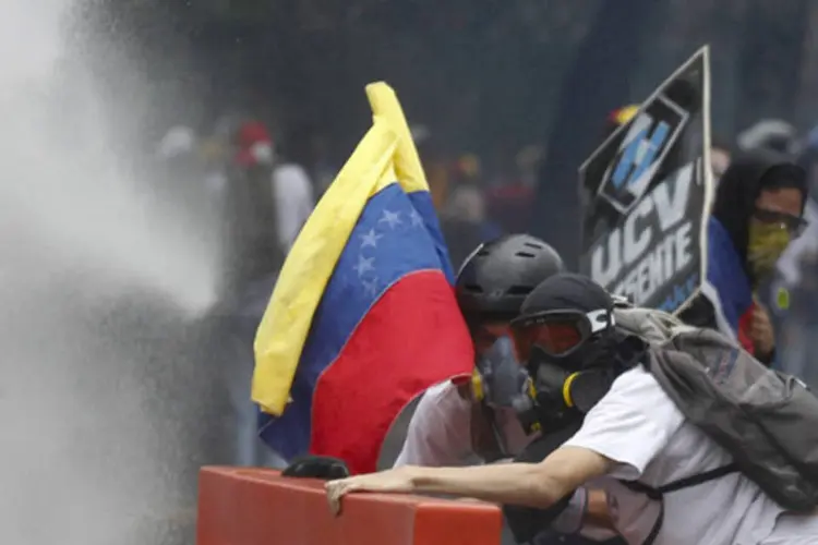 Estudantes venezuelanos se protegem de um canhão d'água durante uma manifestação contra o governo de Nicolás Maduro, em Caracas (Christian Veron/Reuters)