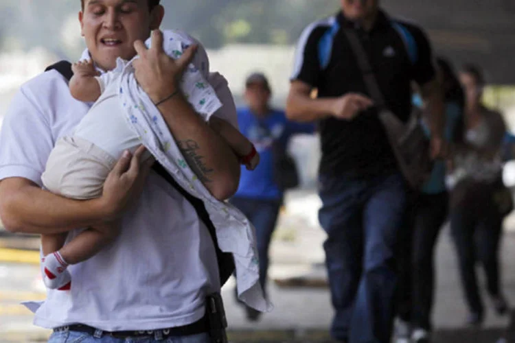 
	Homem tenta proteger beb&ecirc; do g&aacute;s de pimenta lan&ccedil;ado por policiais durante um tumulto em Caracas, na Venezuela
 (Carlos Garcia Rawlins/Reuters)