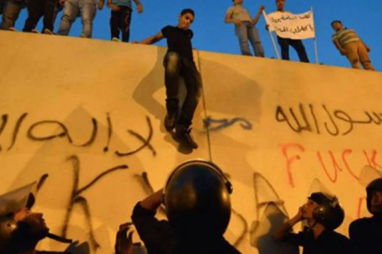 Manifestantes descem de muros da embaixada americana no Cairo observados por policiais: Milhares de pessoas protestaram na terça-feira diante da embaixada dos EUA (©AFP / Khaled Desouki)
