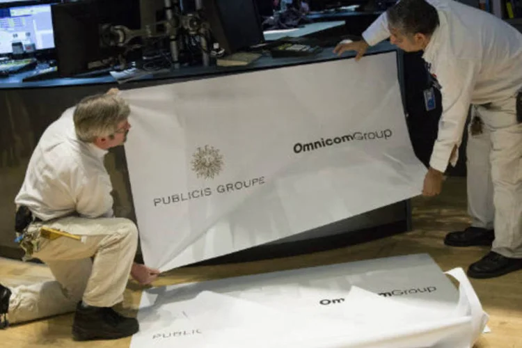Funcionários da Bolsa de Valores de Nova York arrumam banner com os logos do Publicis Groupe e do Omnicom Group após o anúncio de fusão das duas empresas (Scott Eells/Bloomberg)