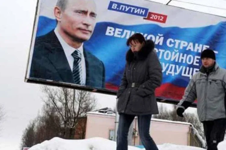 Duas pessoas passam por um cartaz de Vladimir Putin no qual ele diz: "Um grande país, merecem um futuro" em Smolenks, 480 quilômetros de Moscou (Viktor Drachev/AFP)