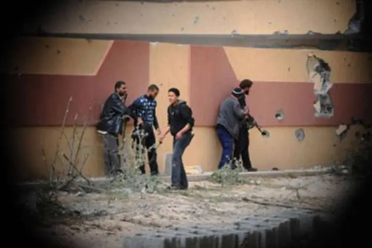 Rebeldes são vistos através de um buraco na parede usado por atirador de elite, enquanto tentam atacar prédio que abriga forças leais ao coronel Muamar Kadhafi (Christophe Simon/AFP)