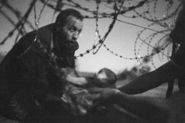 
	Foto ganhadora: o beb&ecirc; passa de m&atilde;o em m&atilde;o sob a cerca de arame farpado instalada entre Horgos, na S&eacute;rvia, e Roszke, na Hungria
 (Warren Richardson / Reuters)