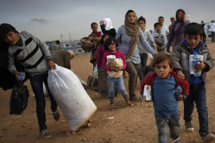 
	Refugiados s&iacute;rios curdos carregam seus pertences ap&oacute;s cruzar fronteira entre Turquia e S&iacute;ria
 (Murad Sezer/Reuters)
