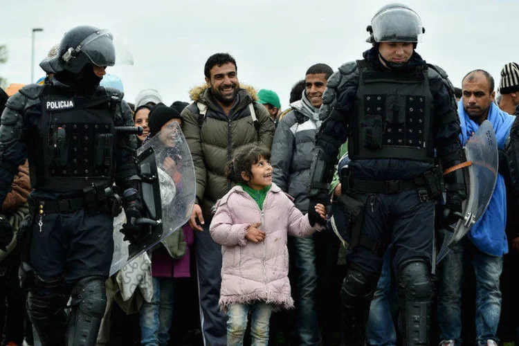 
	Um policial que escoltava um grupo de refugiados da Cro&aacute;cia para a Eslov&ecirc;nia sorri e d&aacute; a m&atilde;o a uma garotinha
 (Getty Images/Jeff J Mitchell)