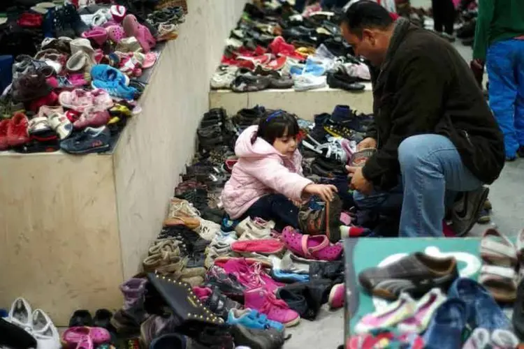 
	Uma menina acompanhada de um adulto escolhe sapatos, ap&oacute;s chegar &agrave; Alemanha
 (Reuters)