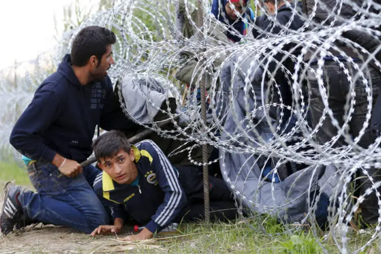
	Refugiados s&iacute;rios atravessam uma cerca na Hungria: o chefe do governo h&uacute;ngaro foi contra a proposta do presidente da Comiss&atilde;o Europeia, Jean-Claude Juncker, de acolher e distribuir pela Uni&atilde;o Europeia 160 mil refugiados
 (REUTERS)