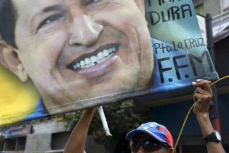 
	Homem segura retrato de Ch&aacute;vez: pessoas empunhando bandeiras venezuelanas faziam fila para visita o Quartel da Montanha
 (Raul Arboleda/AFP)