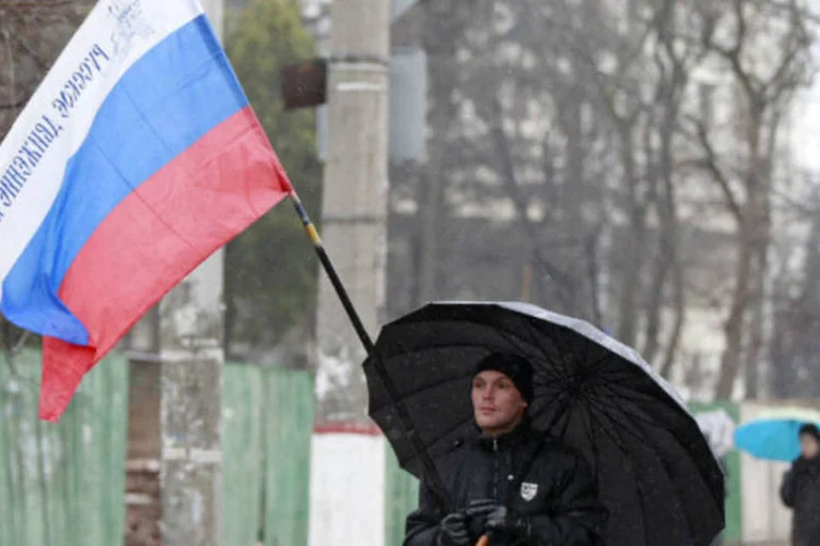 
	Homem com a bandeira da R&uacute;ssia na Crimeia: Crimeia est&aacute; povoada por 2 milh&otilde;es de pessoas (60% s&atilde;o russos, 26% ucranianos e 12% t&aacute;rtaros, favor&aacute;veis a manter a regi&atilde;o dentro da Ucr&acirc;nia)
 (David Mdzinarishvili/AFP)