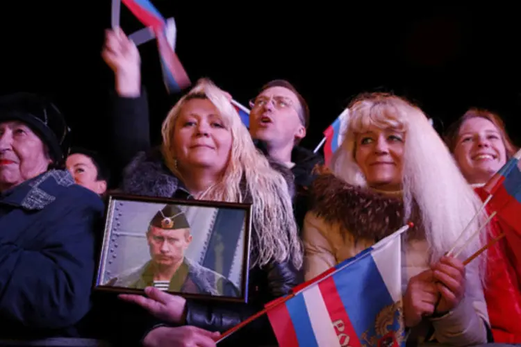 
	Mulher segura foto do presidente russo Vladimir Putin junto a outros cidad&atilde;os que comemoram resultados preliminares do referendo sobre uni&atilde;o da Crimeia &agrave; R&uacute;ssia
 (REUTERS/Baz Ratner)