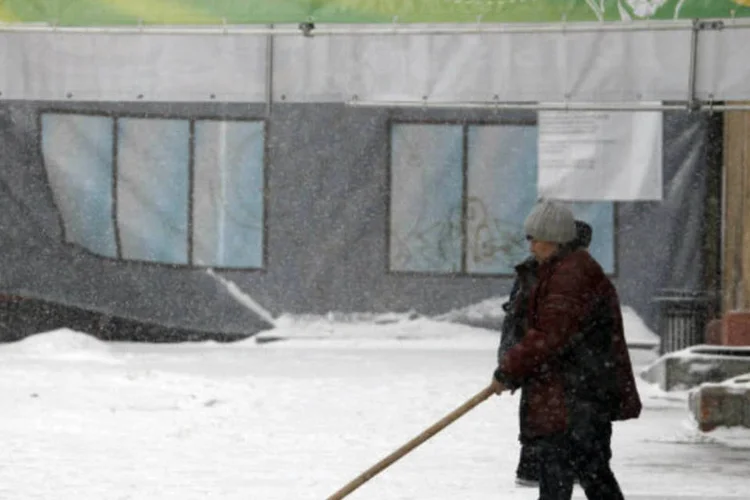 Mulher remove neve em Moscou, com a temperatura do ar em cerca de menos 6 graus Celsius: banner de publicidade de um café diz "Primavera! Onde está você?" (Sergei Karpukhin/Reuters)