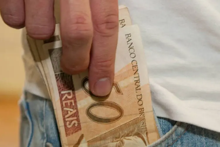 Pessoa retira dinheiro do bolso - notas de cinquenta reais (Marcos Santos/USP Imagens)