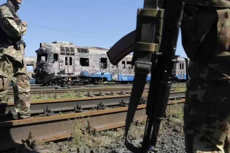 
	Separatistas pr&oacute;-R&uacute;ssia diante de trens destru&iacute;dos na cidade ucraniana de Ilovaysk, no domingo
 (Maxim Shemetov/Reuters)