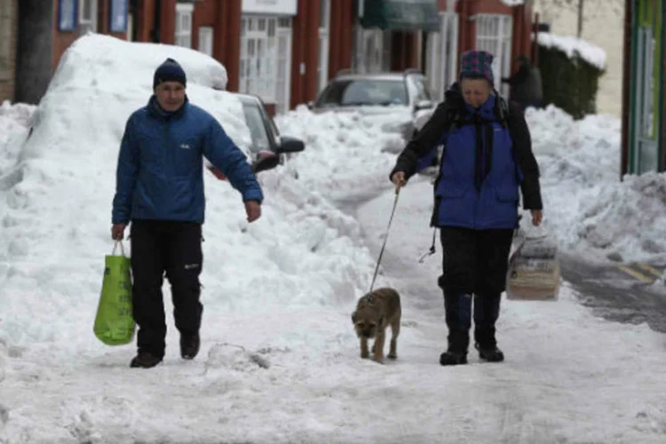 Pessoas carregam sacolas de compras por uma rua coberta de neve em Llangollen, na Sibéria (REUTERS / Phil Noble)