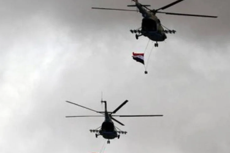 Helicóptero do exército sírio sobrevoa manifestação pró-regime com bandeiras do país (©AFP / Louai Beshara)
