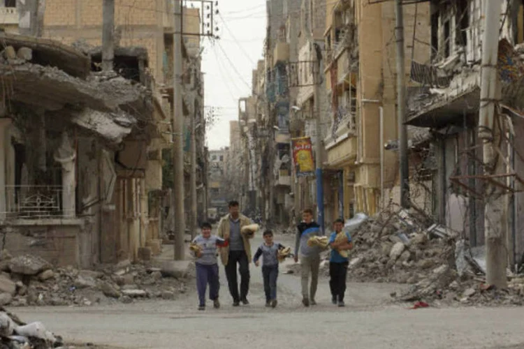 Moradores caminham em rua de Deir al-Zor, na Síria, depois de receberem comida de organizações humanitárias na cidade (REUTERS / Khalil Ashawi)
