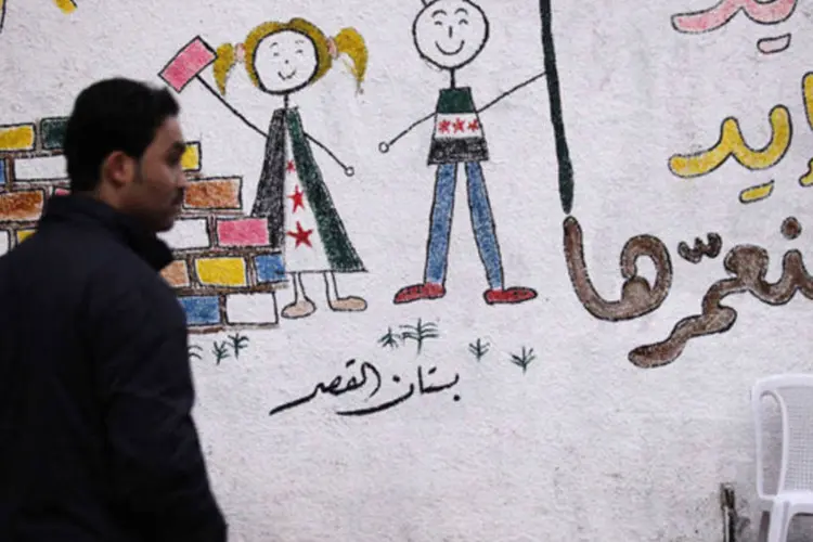 Homem caminha em frente a um grafite onde se lê em árabe "Suas mãos e minhas mãos podem juntas reconstruir nosso país" (Zain Karam/Reuters)