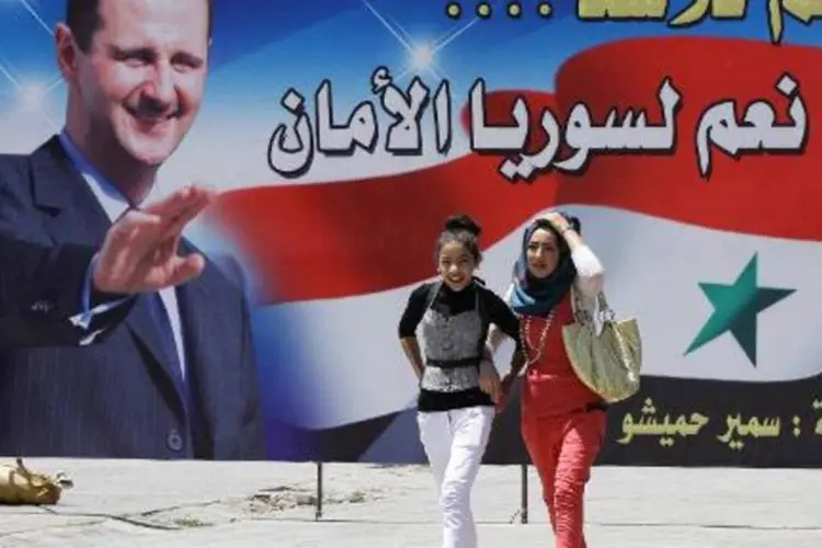 
	S&iacute;rias passam em frente a cartaz de Bashar al-Assad: elei&ccedil;&atilde;o ser&aacute; em 03 de junho
 (Louai Beshara/AFP)