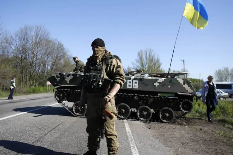 Um soldado ucraniano fica de guarda em frente a um veículo blindado em um posto de controle na vila de Malinivka, perto de Slaviansk, no leste da Ucrânia (Marko Djurica/Reuters)