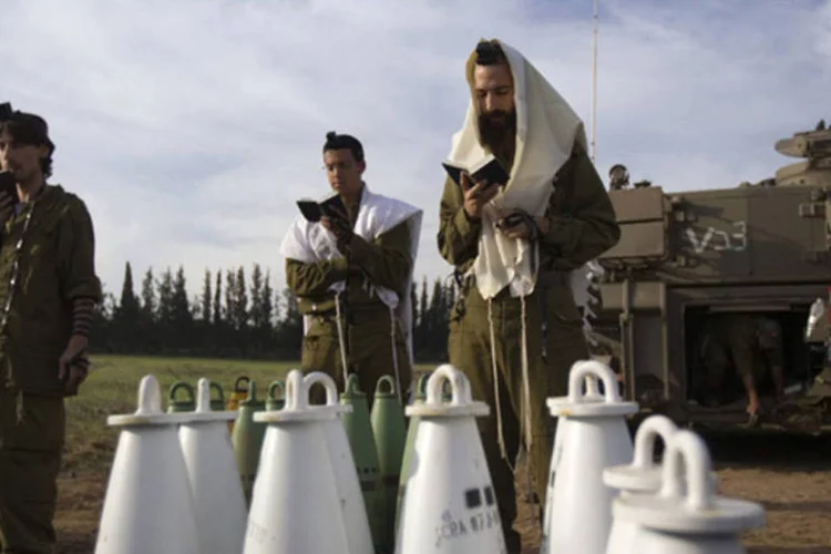 
	Soldados israelenses rezam em frente a armamentos na fronteira norte de Israel com a Faixa de Gaza
 (Ronen Zvulun/Reuters)