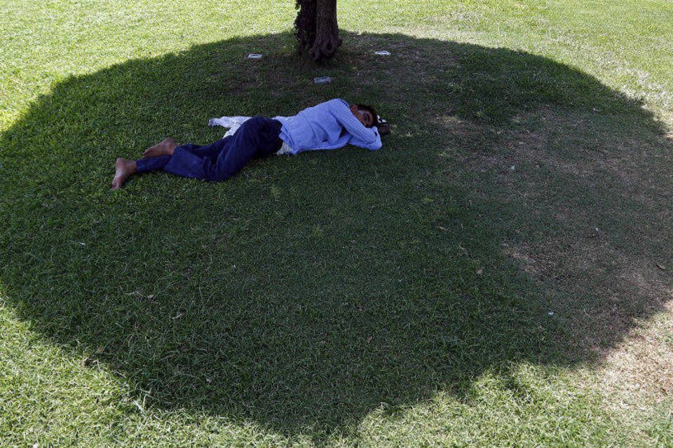 
	Homem dorme em sombra de &aacute;rvore em parque p&uacute;blico de Nova Deli
 (Anindito Mukherjee/Reuters)