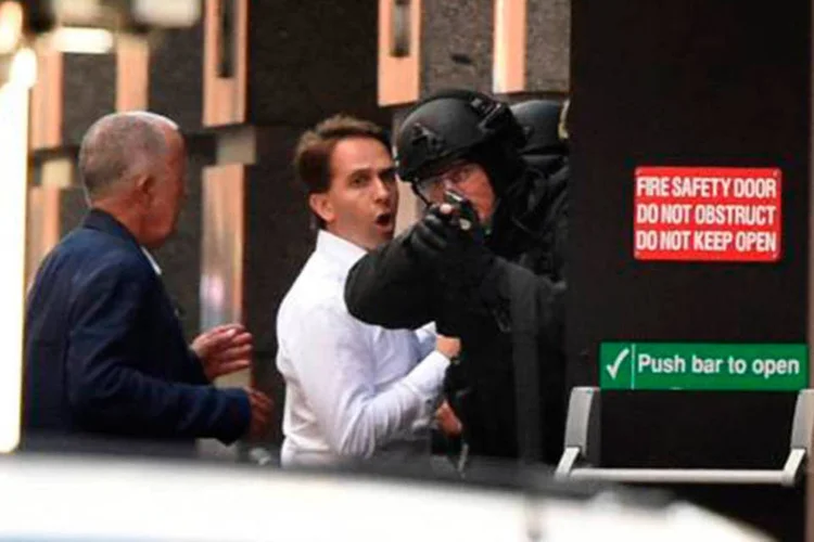 Reféns se protegem atrás de um policial, antes da invasão do café
 (William West/AFP)
