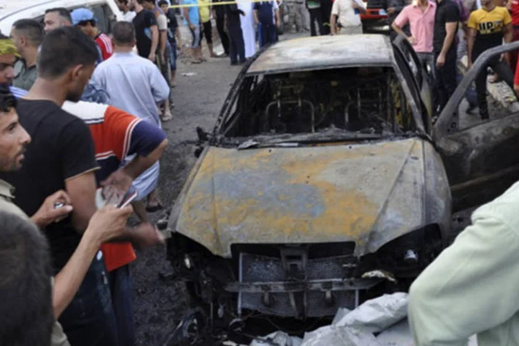 Pessoas reunidas em volta de um carro bomba na cidade de Kut, sudeste de Bagdá: pelo menos 27 pessoas morreram ontem em uma onda de atentados com carros-bomba em áreas com maioria xiita (Jaafer Abed/Reuters)