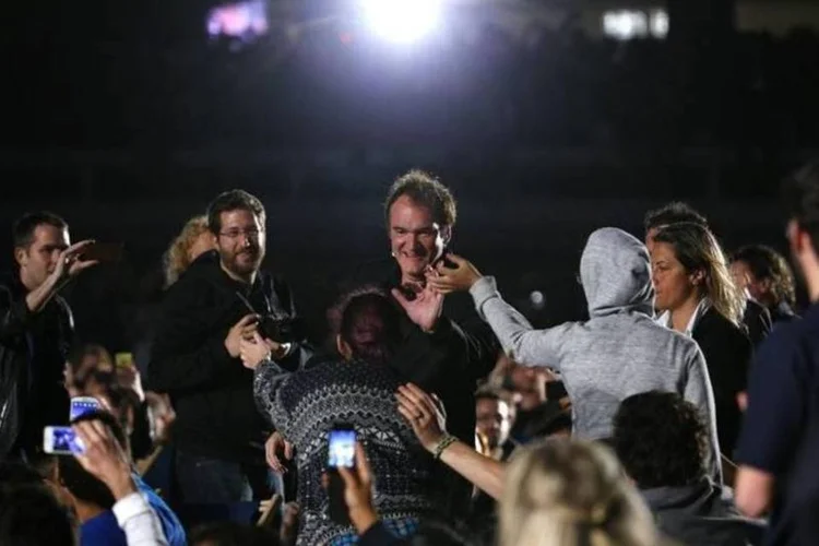 O cineasta Quentin Tarantino (centro) acena para fãs ao chegar à praia para a exibição do seu filme "Pulp Fiction", durante o Festival de Cannes, na França, nesta sexta-feira (Yves Herman/Reuters)